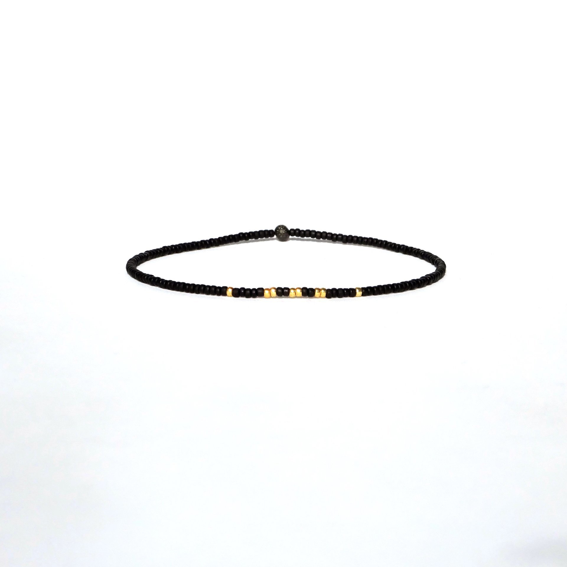A thin minimalist style miyuki stretch bracelet in matte black and gold color